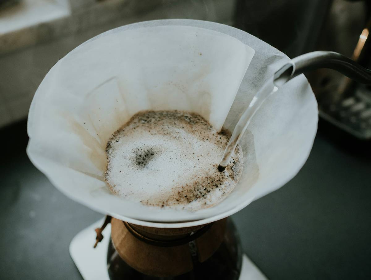 Stainless steel reusable removable coffee filter placed beside fresh coffee grounds and mug